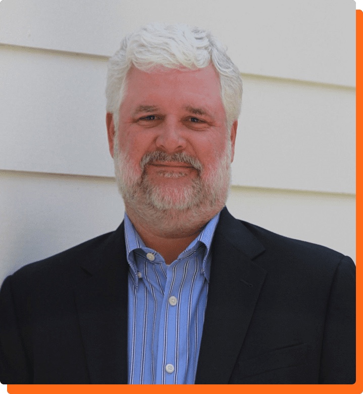 Jack Calhoun, Founder of Encore Career Lab — silver hair and beard, blue button-down shirt, soft natural light, standing in front of his Atlanta home.