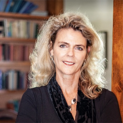 Tavi Meketon, Lead Coach — wavy blonde hair, black top, photographed in front of a home library.